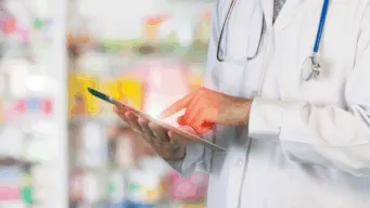 mid-shot of medical person or pharmacist using a tablet with shelves of medications in background showing importance of devsecops processes