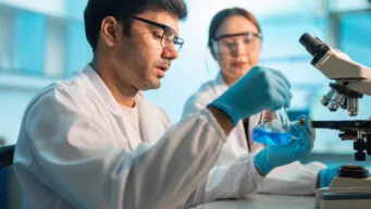 Lab techs working with a beaker and microscope