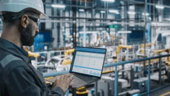 a man standing in a warehouse with a helmet on looking at a laptop