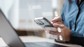 close up of hand using a phone in front of a laptop