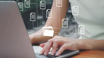 A female worker's hands at a laptop keyboard with file and connectivity icons floating above it indicating the latest B2B integration Essentials updates: automated EDI workflows, expanded trading partner support, and multilingual tools built for growing SMBs.
