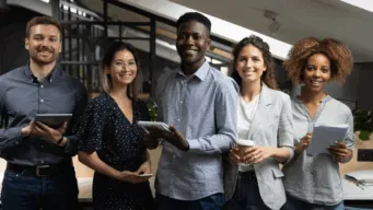 group of 5 diverse developers, each holding a device, smiling into the camera to celebrate National Developers Day, a day that focuses on developer experience (DevEx)